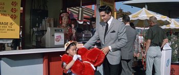 Movie still from “It Happened at the World's Fair” (1963), directed by Norman Taurog – A man and a little girl holding a large red teddy bear; Medium shot, Over the shoulder angle