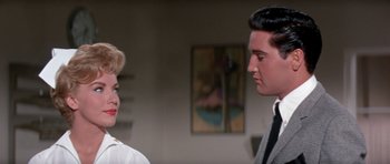 Movie still from “It Happened at the World's Fair” (1963), directed by Norman Taurog – A man and a woman standing next to each other in a room; Medium shot, Over the shoulder angle