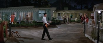 Movie still from “It Happened at the World's Fair” (1963), directed by Norman Taurog – A man walking in a parking lot holding a guitar; Wide shot, High angle