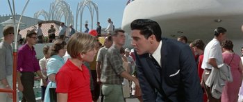 Movie still from “It Happened at the World's Fair” (1963), directed by Norman Taurog – A man in a business suit talking to a young boy in a red shirt; Medium shot, Over the shoulder angle