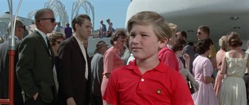 Movie still from “It Happened at the World's Fair” (1963), directed by Norman Taurog – A boy in a red shirt is standing in front of a group of people; Close Up shot, Low angle