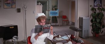 Movie still from “It Happened at the World's Fair” (1963), directed by Norman Taurog – A woman in a nurse's uniform is reading a book; Medium shot, High angle