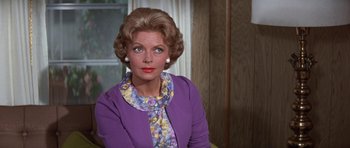 Movie still from “It Happened at the World's Fair” (1963), directed by Norman Taurog – An older woman wearing a purple jacket and a floral scarf; Close Up shot, Over the shoulder angle