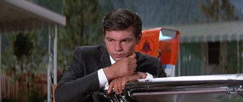 Movie still from “It Happened at the World's Fair” (1963), directed by Norman Taurog – A man in a suit leaning on a car; Close Up shot, Low angle