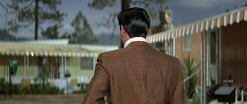 Movie still from “It Happened at the World's Fair” (1963), directed by Norman Taurog – A man wearing a suit and tie standing in front of a trailer; Medium shot, Over the shoulder angle