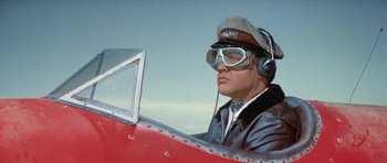 Movie still from “It Happened at the World's Fair” (1963), directed by Norman Taurog – A man in a pilot's hat and goggles sitting in an airplane cockpit; Medium shot, Low angle