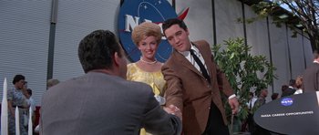 Movie still from “It Happened at the World's Fair” (1963), directed by Norman Taurog – A man and a woman shaking hands in front of a nasa sign; Medium shot, Low angle