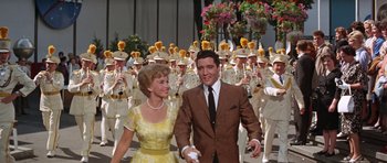 Movie still from “It Happened at the World's Fair” (1963), directed by Norman Taurog – A man and a woman are walking in front of a group of people; Medium shot, Low angle