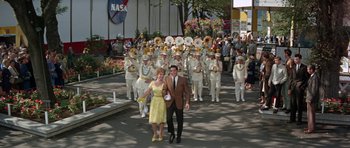 Movie still from “It Happened at the World's Fair” (1963), directed by Norman Taurog – A man and a woman are walking in front of a marching band; Wide shot, Low angle