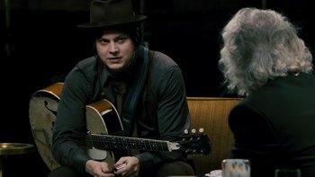 Movie still from “It Might Get Loud” (2008), directed by Davis Guggenheim – A man sitting on a couch holding a guitar; Medium shot, Over the shoulder angle
