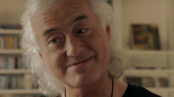Movie still from “It Might Get Loud” (2008), directed by Davis Guggenheim – An older man with white curly hair smiling for the camera; Close Up shot, Over the shoulder angle