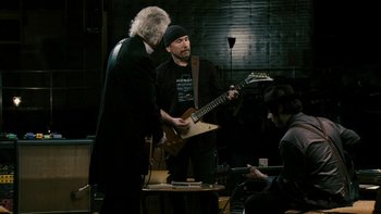 Movie still from “It Might Get Loud” (2008), directed by Davis Guggenheim – A man playing a guitar while another man watches; Medium shot, Over the shoulder angle