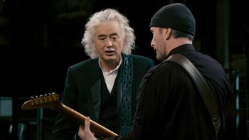 Movie still from “It Might Get Loud” (2008), directed by Davis Guggenheim – A man holding an electric guitar talking to another man; Medium shot, Over the shoulder angle