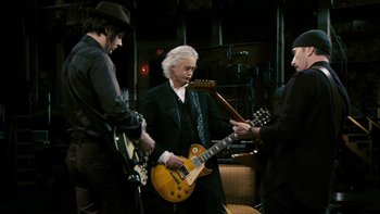 Movie still from “It Might Get Loud” (2008), directed by Davis Guggenheim – A group of men standing next to each other holding guitars; Medium shot, Low angle