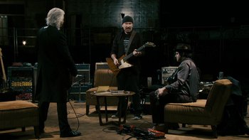 Movie still from “It Might Get Loud” (2008), directed by Davis Guggenheim – A group of people that are sitting in a living room; Wide shot, Over the shoulder angle