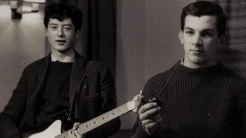 Movie still from “It Might Get Loud” (2008), directed by Davis Guggenheim – Two young men standing next to each other holding a guitar; Medium shot, Low angle