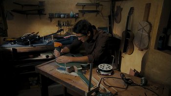 Movie still from “It Might Get Loud” (2008), directed by Davis Guggenheim – A man working on a guitar in a workshop; Medium shot, High angle
