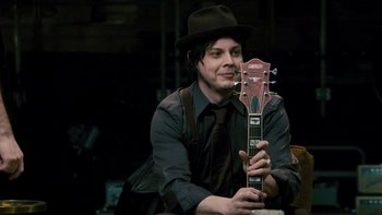 Movie still from “It Might Get Loud” (2008), directed by Davis Guggenheim – A man in a hat holding up a guitar; Medium shot, High angle