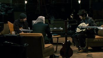 Movie still from “It Might Get Loud” (2008), directed by Davis Guggenheim – A group of people sitting around a room with guitars; Wide shot, High angle