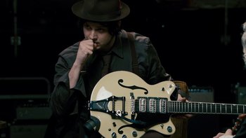 Movie still from “It Might Get Loud” (2008), directed by Davis Guggenheim – A man in a hat is holding a guitar; Medium shot, High angle