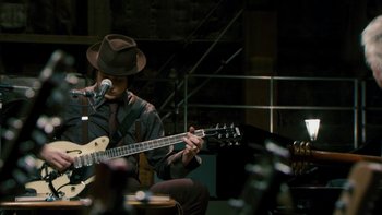 Movie still from “It Might Get Loud” (2008), directed by Davis Guggenheim – A man in a hat playing a guitar in front of a microphone; Medium shot, High angle