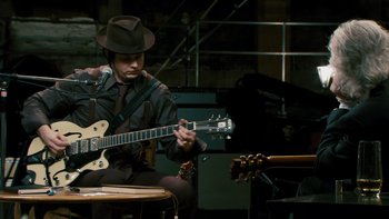 Movie still from “It Might Get Loud” (2008), directed by Davis Guggenheim – A man in a hat playing an electric guitar in front of a microphone; Medium shot, High angle