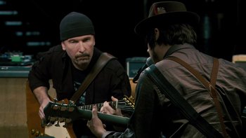 Movie still from “It Might Get Loud” (2008), directed by Davis Guggenheim – A man playing a guitar while another man looks on; Close Up shot, Over the shoulder angle