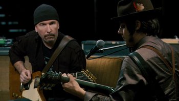 Movie still from “It Might Get Loud” (2008), directed by Davis Guggenheim – A man playing a guitar while another man looks on; Close Up shot, Over the shoulder angle