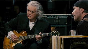 Movie still from “It Might Get Loud” (2008), directed by Davis Guggenheim – A man in a black suit playing an electric guitar; Medium shot, Over the shoulder angle