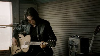 Movie still from “It Might Get Loud” (2008), directed by Davis Guggenheim – A man in a black jacket playing an electric guitar; Medium shot, Low angle