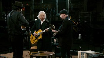 Movie still from “It Might Get Loud” (2008), directed by Davis Guggenheim – A man playing a guitar while another man looks on; Medium shot, Low angle