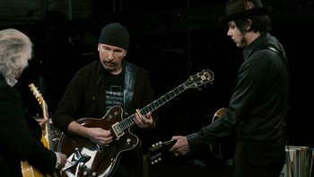 Movie still from “It Might Get Loud” (2008), directed by Davis Guggenheim – A man playing a guitar while another man holds a guitar; Medium shot, Low angle