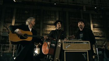 Movie still from “It Might Get Loud” (2008), directed by Davis Guggenheim – A group of people that are standing around a guitar; Medium shot, Low angle