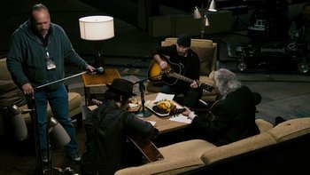 Movie still from “It Might Get Loud” (2008), directed by Davis Guggenheim – A group of men sitting around a table playing instruments; Wide shot, High angle