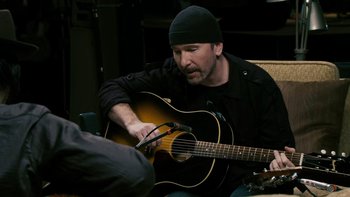 Movie still from “It Might Get Loud” (2008), directed by Davis Guggenheim – A man sitting down playing an acoustic guitar; Medium shot, Over the shoulder angle