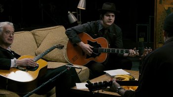 Movie still from “It Might Get Loud” (2008), directed by Davis Guggenheim – A man sitting on top of a couch playing a guitar; Medium shot, High angle