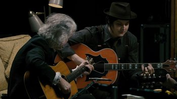 Movie still from “It Might Get Loud” (2008), directed by Davis Guggenheim – A man playing an instrument while another man plays a guitar; Medium shot, Over the shoulder angle