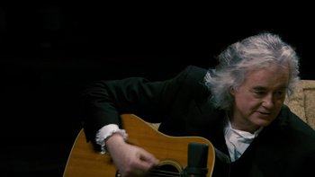 Movie still from “It Might Get Loud” (2008), directed by Davis Guggenheim – An older person playing a guitar in a dark room; Close Up shot, Low angle