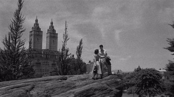 Movie still from “It Should Happen to You” (1954), directed by George Cukor – A man and a woman sitting on top of a rock; Extreme Wide shot, High angle