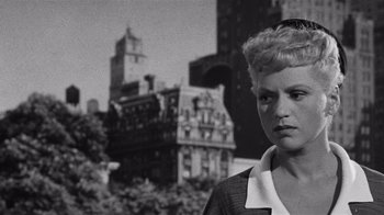 Movie still from “It Should Happen to You” (1954), directed by George Cukor – A black - and - white photo of a woman in front of buildings; Close Up shot, Low angle