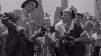 Movie still from “It Should Happen to You” (1954), directed by George Cukor – An old black and white photo of a woman taking a picture; Medium shot, High angle