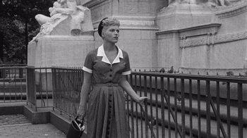Movie still from “It Should Happen to You” (1954), directed by George Cukor – An old photo of a woman in a dress standing next to a fence; Medium shot, Low angle