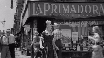 Movie still from “It Should Happen to You” (1954), directed by George Cukor – An older woman walking down the street in front of a store; Wide shot, Low angle