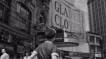 Movie still from “It Should Happen to You” (1954), directed by George Cukor – A black - and - white photo of a woman walking down the street; Wide shot, Low angle
