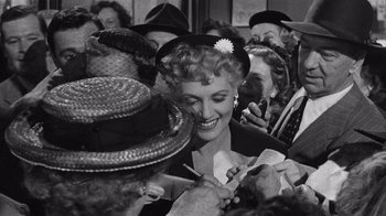 Movie still from “It Should Happen to You” (1954), directed by George Cukor – An old black and white photo of a woman in a crowd; Medium shot, High angle