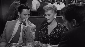 Movie still from “It Should Happen to You” (1954), directed by George Cukor – A man and a woman sitting at a table with another man; Medium shot, Over the shoulder angle