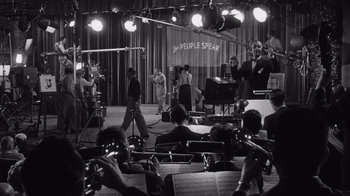 Movie still from “It Should Happen to You” (1954), directed by George Cukor – A black and white photo of a group of people in front of microphones; Extreme Wide shot, High angle