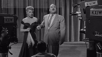 Movie still from “It Should Happen to You” (1954), directed by George Cukor – A man and a woman standing next to each other on a stage; Medium shot, Over the shoulder angle