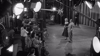 Movie still from “It Should Happen to You” (1954), directed by George Cukor – A black - and - white photo of a man and a woman in front of a camera; Wide shot, High angle