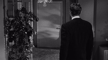 Movie still from “It Should Happen to You” (1954), directed by George Cukor – A black and white photo of a man standing in front of an open door; Medium shot, Over the shoulder angle